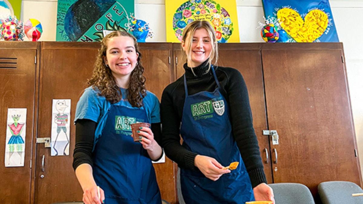 two female students pose with paintbrushes in hand