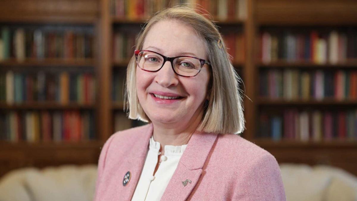 Image of President Getz smiling and standing in front of a couch and bookshelf