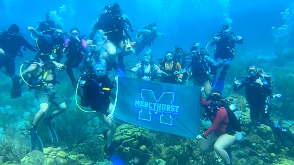 Students holding a Mercyhurst flag underwater in Bonaire