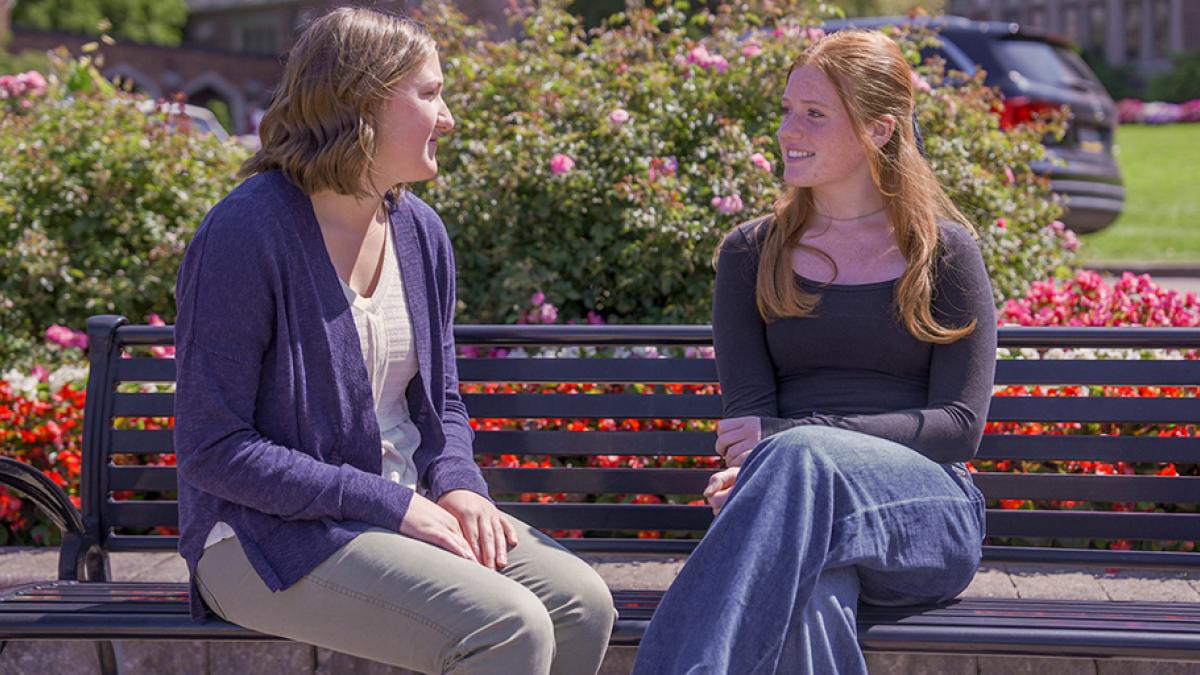 Students sitting on a bench talking in the Mary Garden