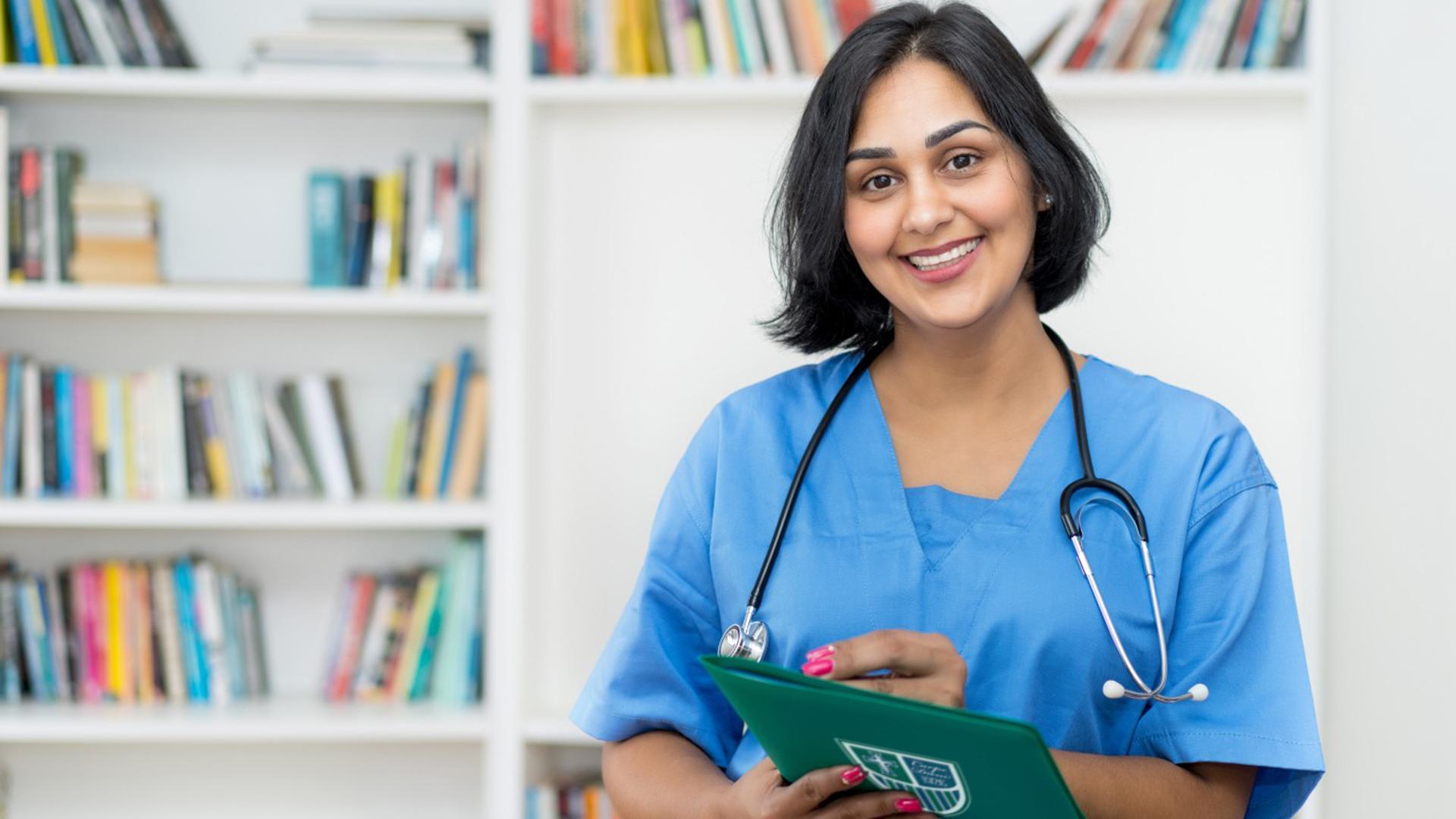 Stock image of an MSN student holding a Mercyhurst folder, standing in front of a bookshelf