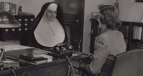 Black and White image of Mother Borgia sitting at a desk, talking to a female in 1938