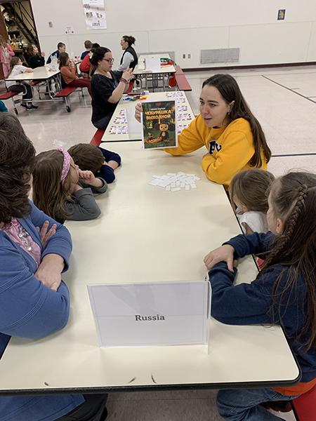 Female showing book to children at a table with a Russia sign